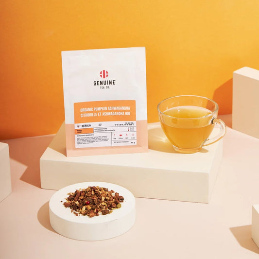 Tea package, cup of tea, and tea leaves on a light pink surface with an orange background