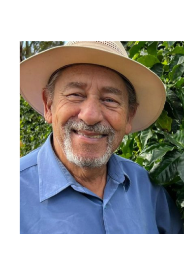 Man wearing a wide-brimmed hat and blue shirt standing in front of coffee plants with green beans.