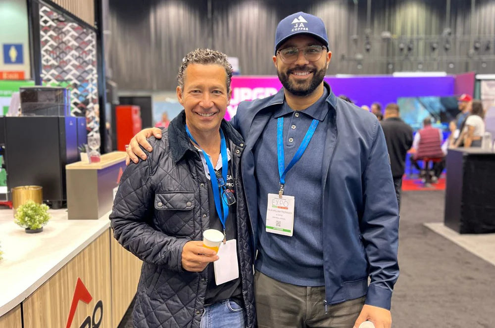 Two men posing together at a convention or event, wearing badges and smiling.