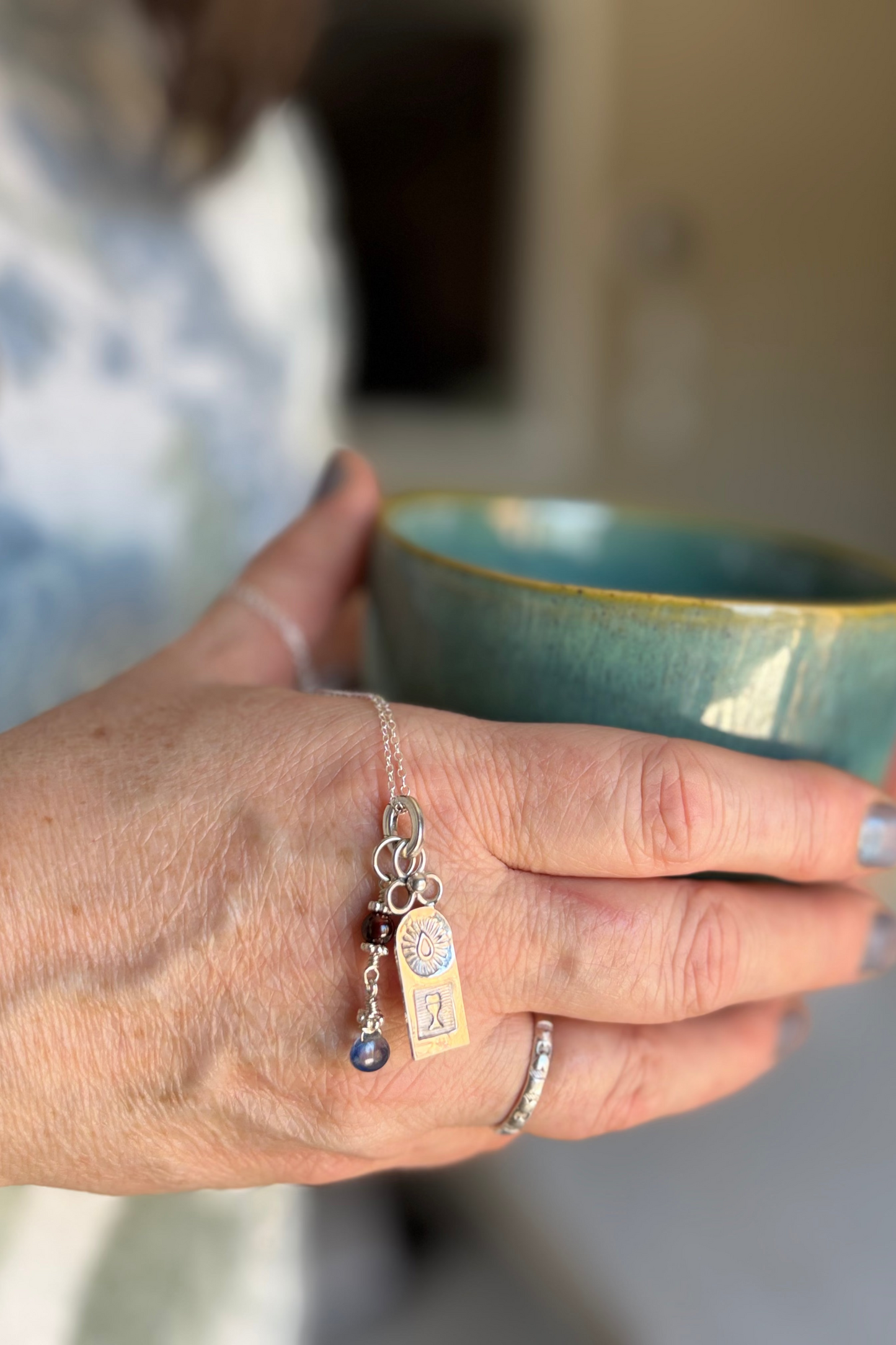 Hand holding a blue ceramic cup & silver necklace with a blurred background