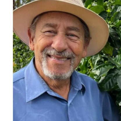 Man wearing a wide-brimmed hat and blue shirt in front of green foliage