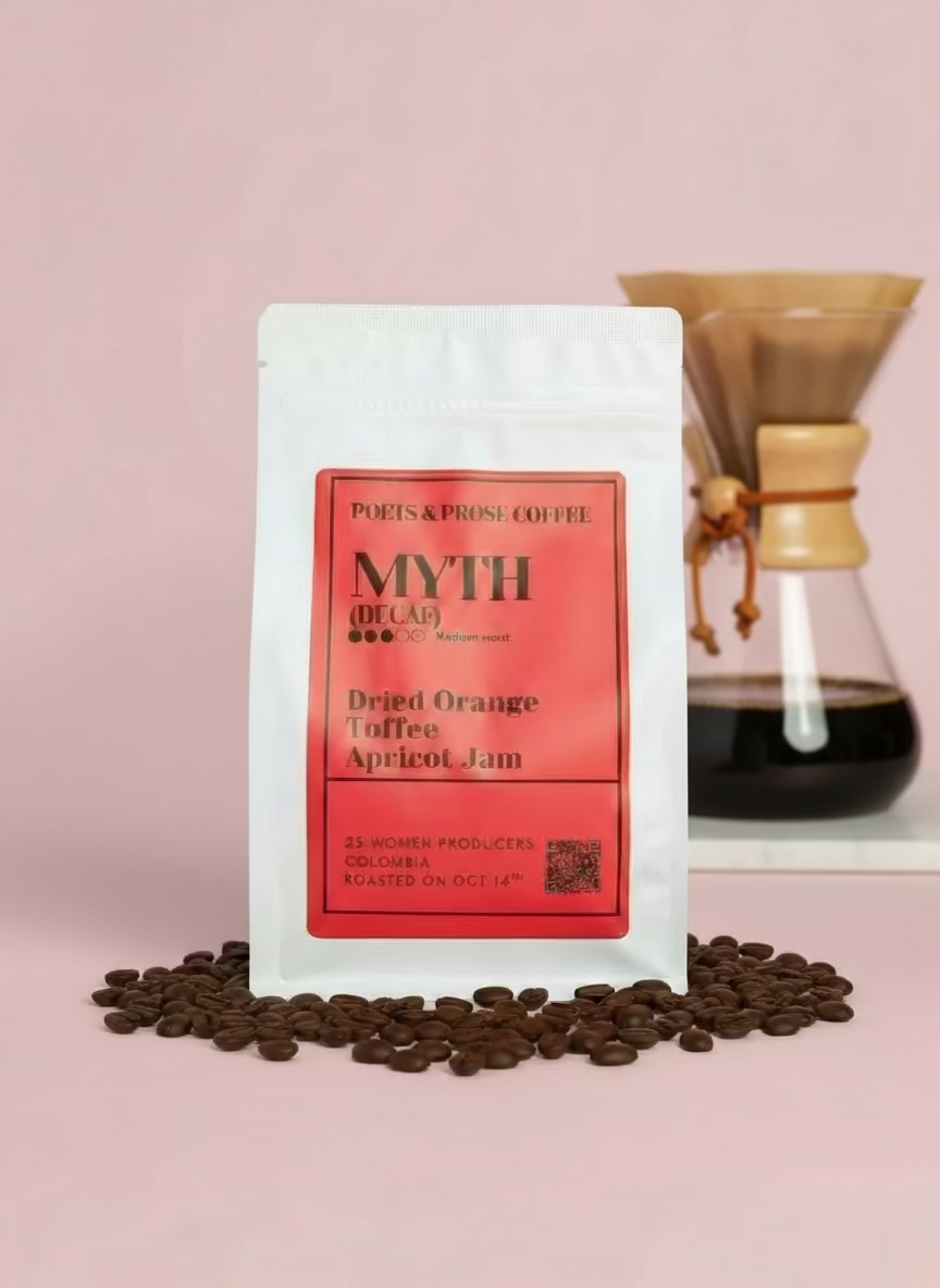 Coffee package with a red label on a pink background, surrounded by coffee beans and dried fruit.